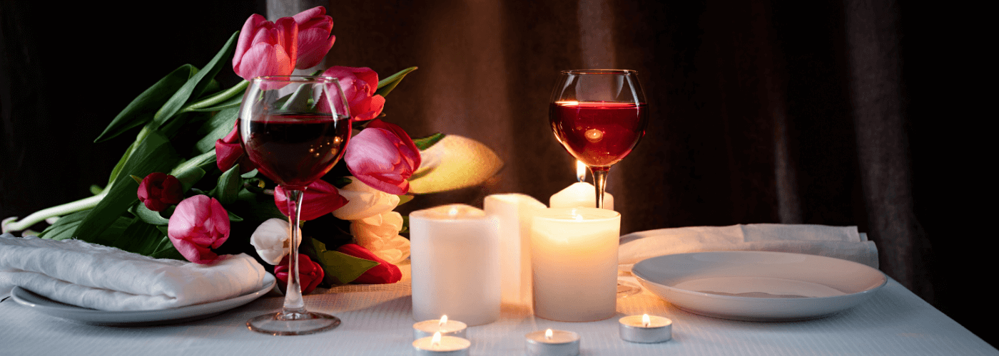 romantic dinner table setting with red tulips, candles, wine glasses & plates on a dark background, creating a warm ambiance