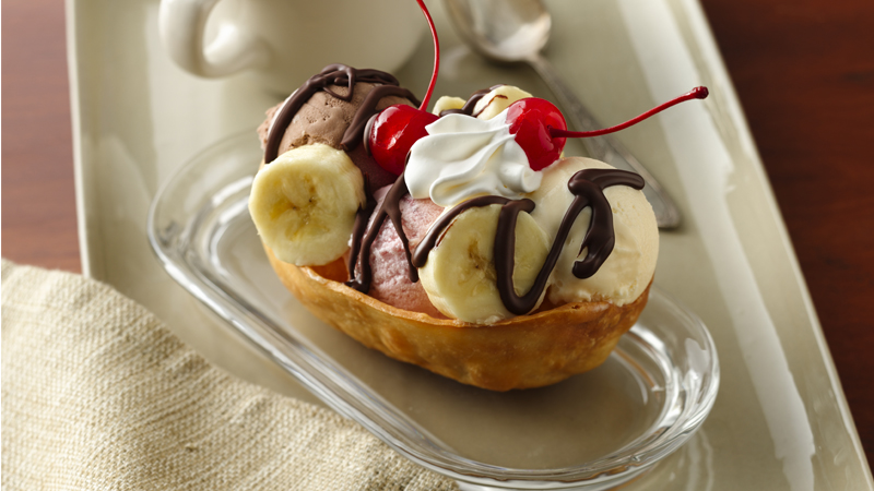 banana split stand n stuff dessert tacos topped with cream & cheery served on a glass plate